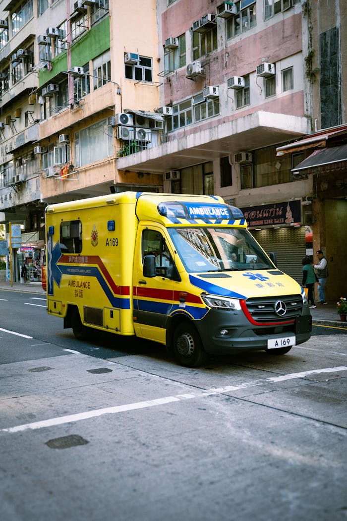 Yellow ambulance on an urban street in front of colorful residential buildings.