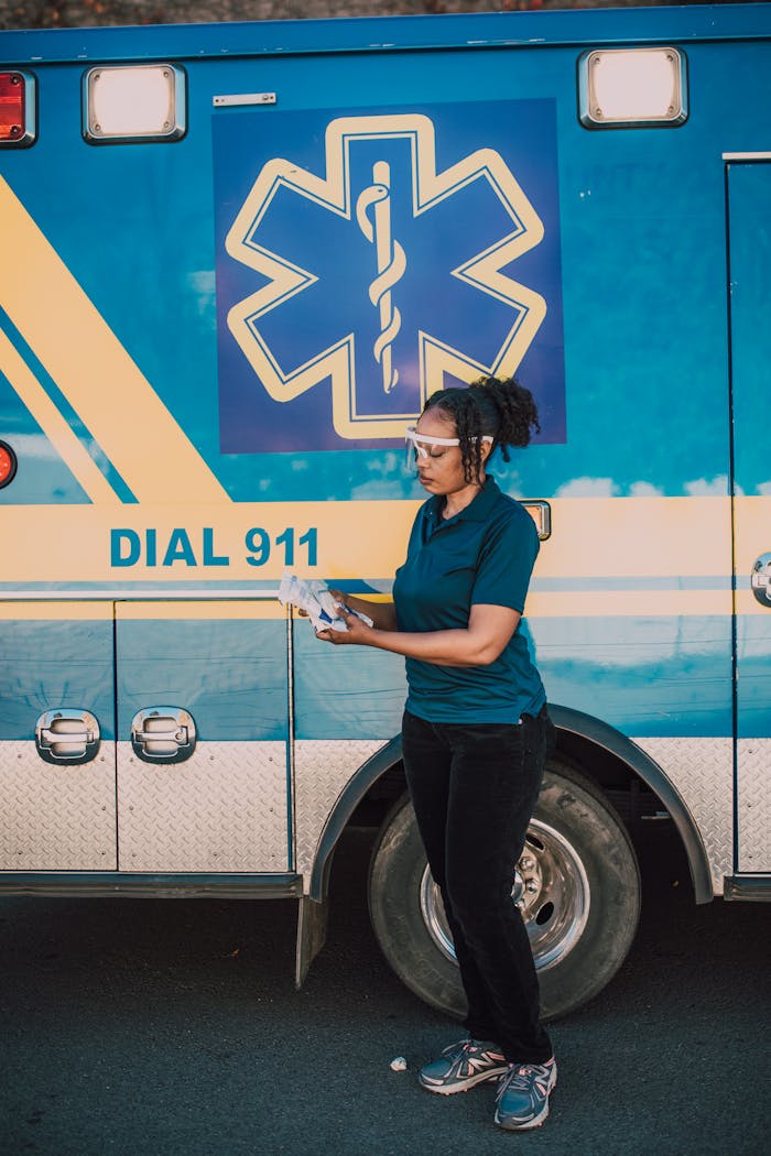 An EMT standing in front of an ambulance holding medical products, ready to respond to emergencies.